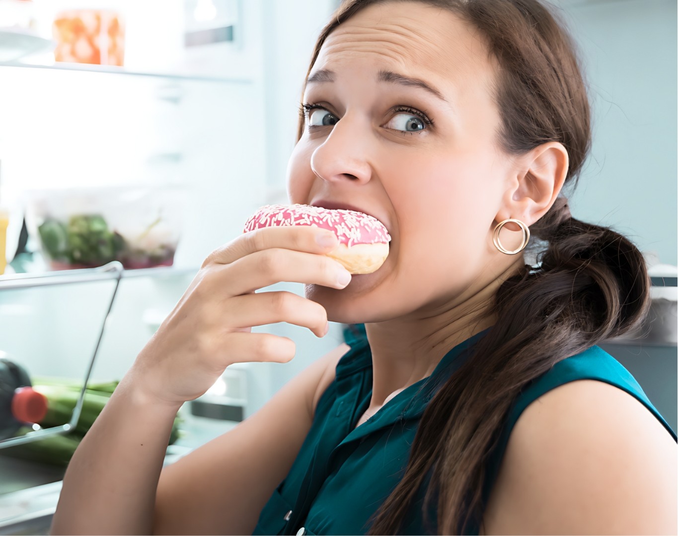 Woman eating a donut near an open refrigerator